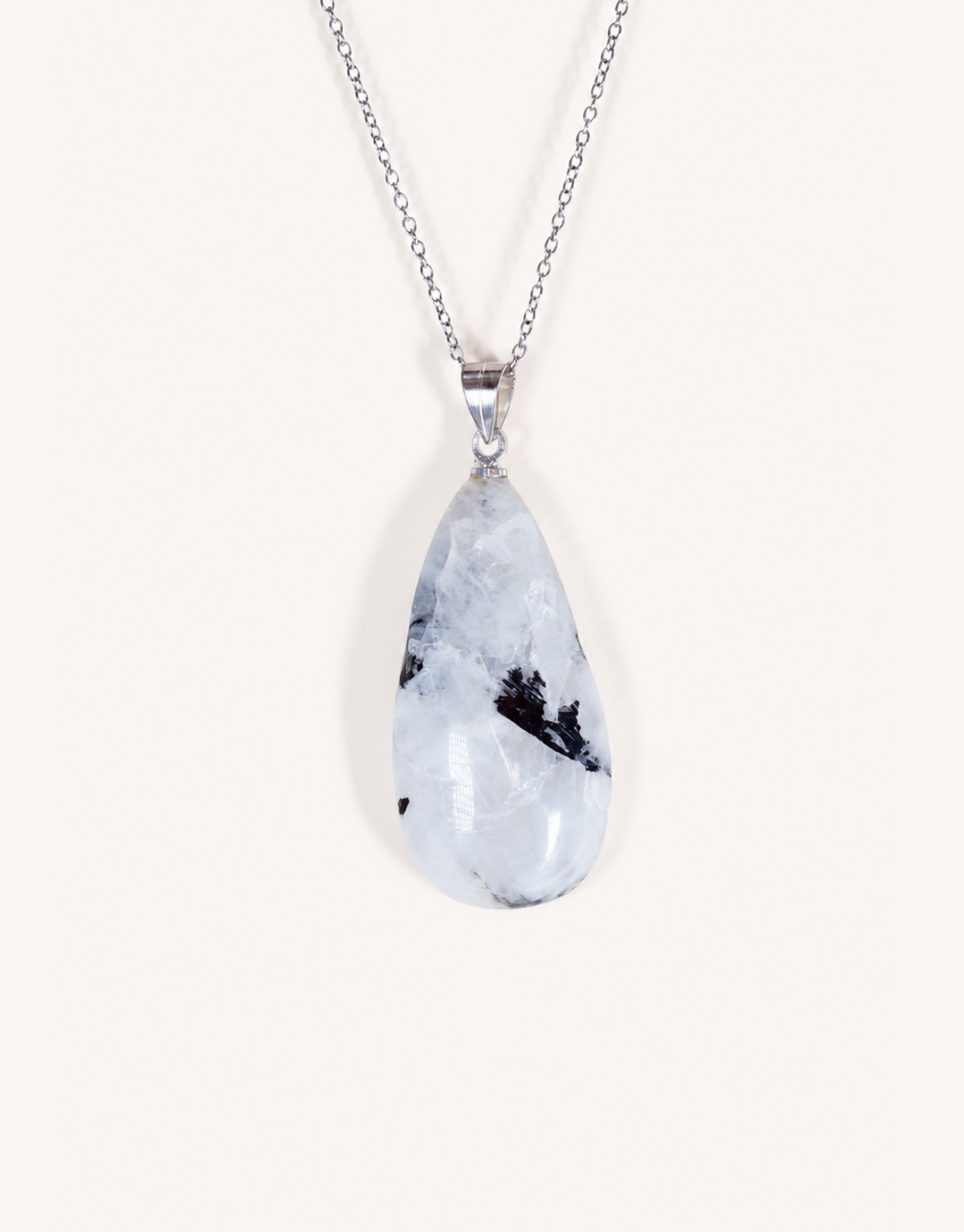 A freeform Natural Moonstone Pendant featuring opaque white stone with black tourmaline inclusions on an 18-inch stainless steel chain.