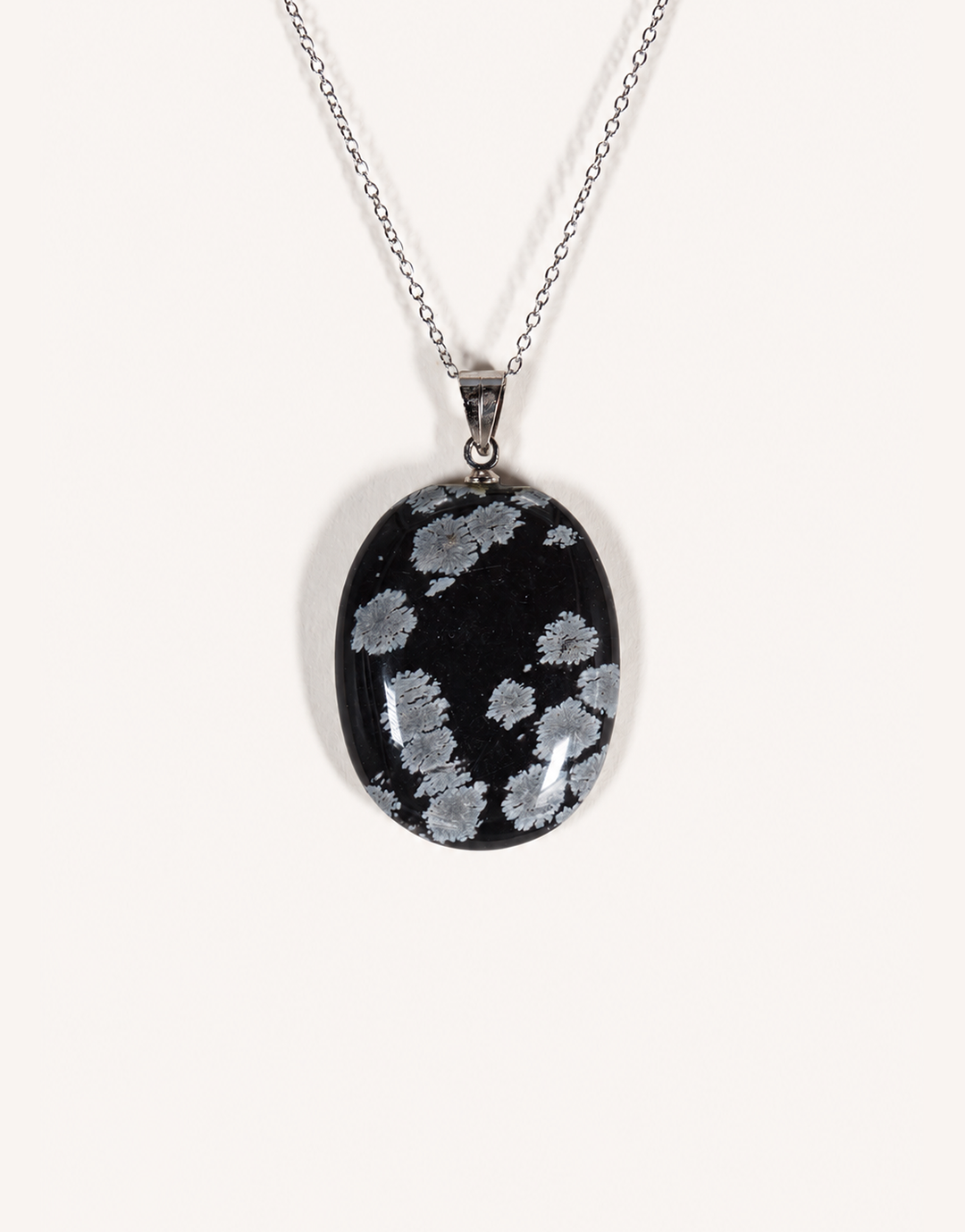 A Natural Snowflake Obsidian Pendant displaying smooth black stone with white cristobalite patches on an 18-inch stainless steel chain.