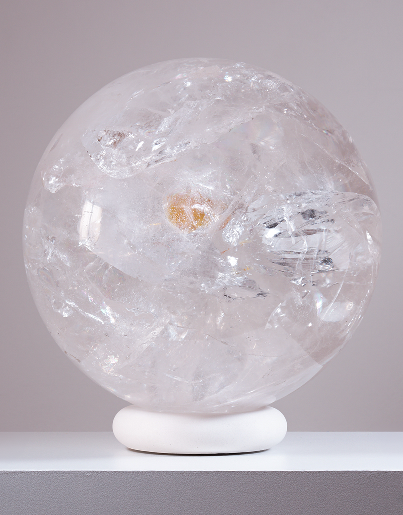 An 8.1 kg Natural Clear Quartz Sphere from Brazil, measuring 20 cm in diameter, displaying light-refracting internal veils on a white stand.