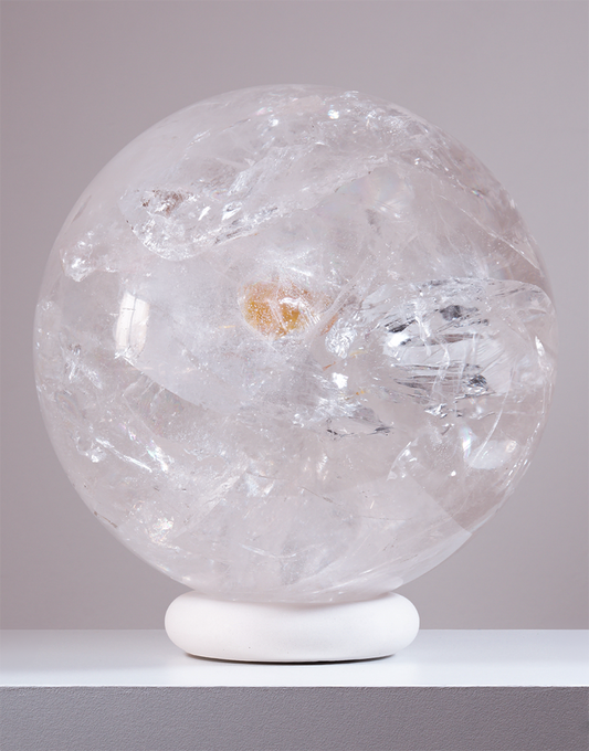 An 8.1 kg Natural Clear Quartz Sphere from Brazil, measuring 20 cm in diameter, displaying light-refracting internal veils on a white stand.