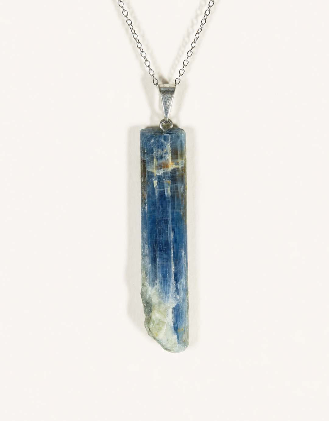 A raw blue kyanite crystal pendant necklace on a silver chain, photographed against a plain off-white background.