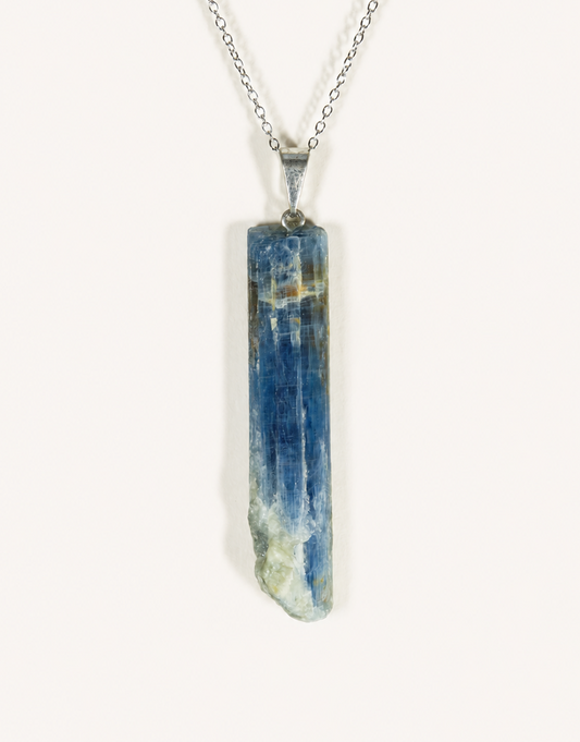 A raw blue kyanite crystal pendant necklace on a silver chain, photographed against a plain off-white background.