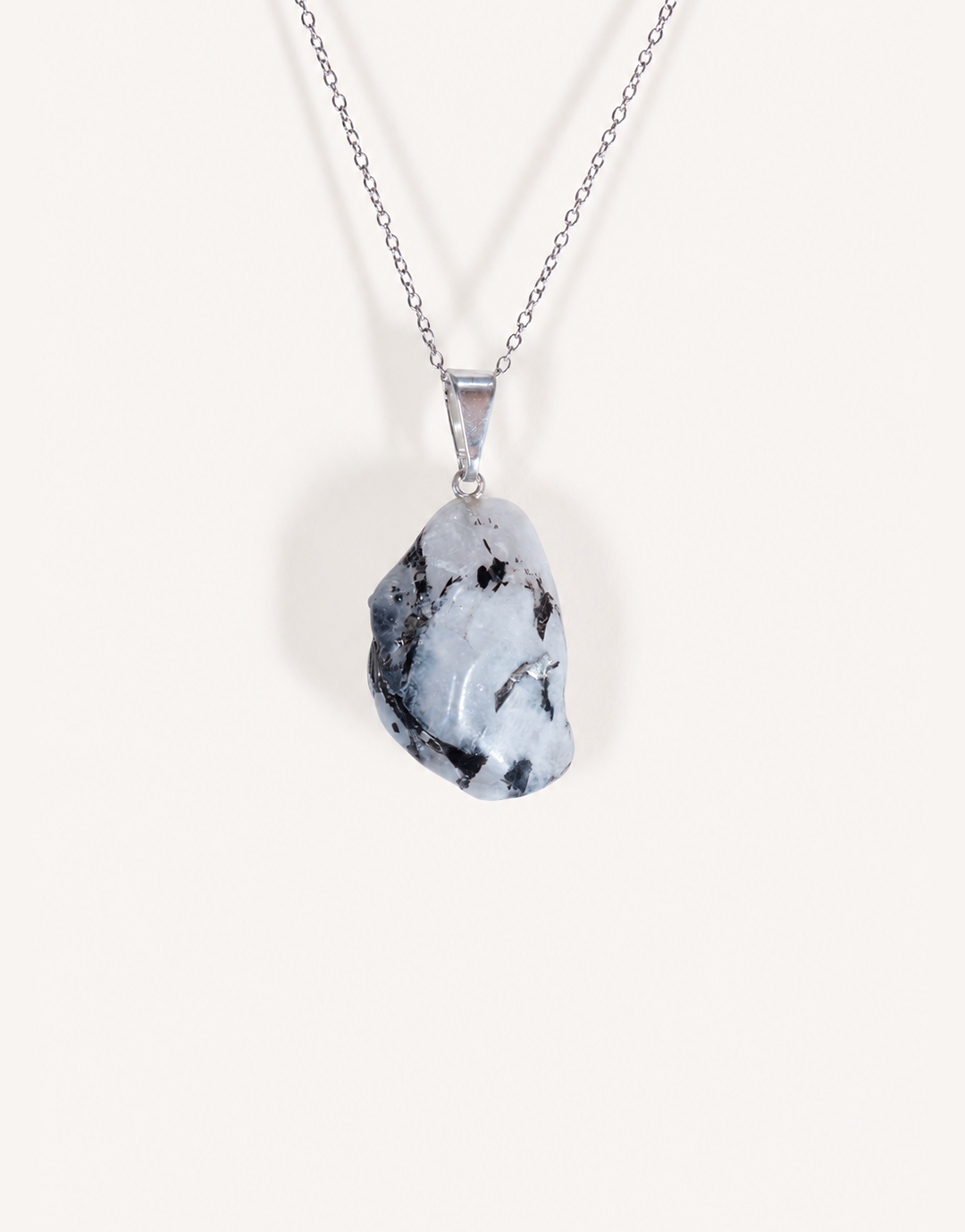 A freeform Natural Moonstone Pendant featuring opaque white stone with black tourmaline matrix spots on an 18-inch stainless steel chain.