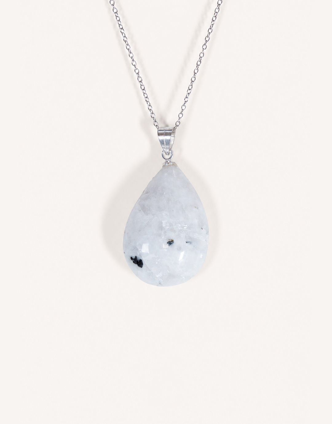 A freeform Natural Moonstone Pendant featuring opaque white stone with black tourmaline inclusions on an 18-inch stainless steel chain.