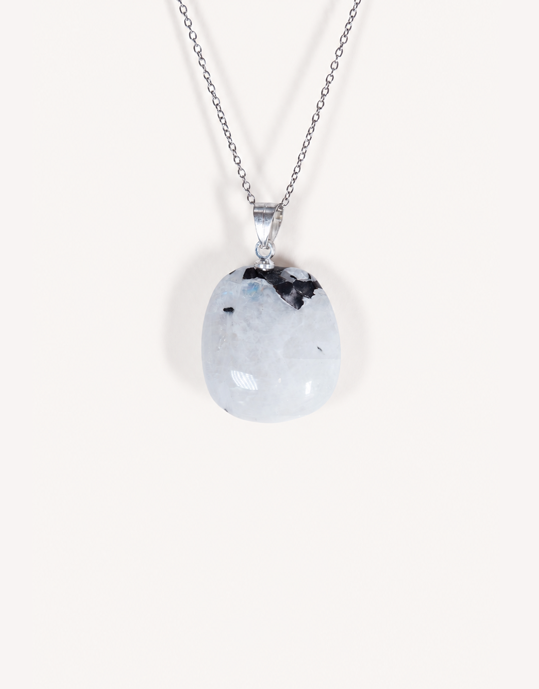 A freeform Natural Moonstone Pendant featuring opaque white stone with black tourmaline inclusions on an 18-inch stainless steel chain.
