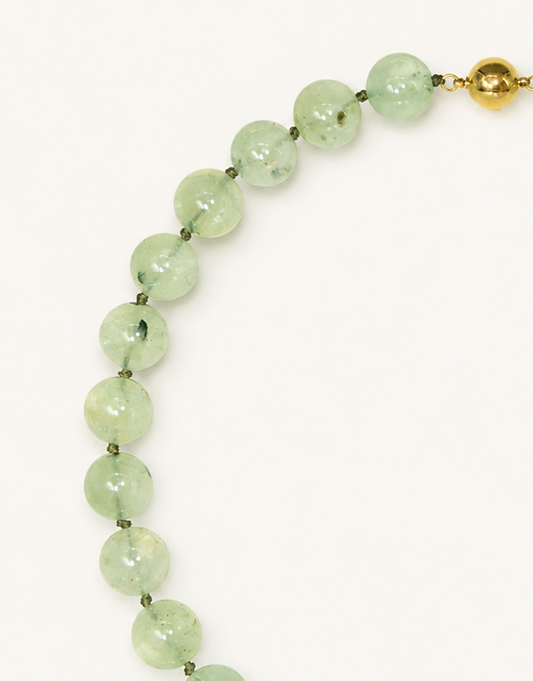 A 16-inch Natural Prehnite Choker featuring polished 12mm light green beads with unique dark tourmaline inclusions.