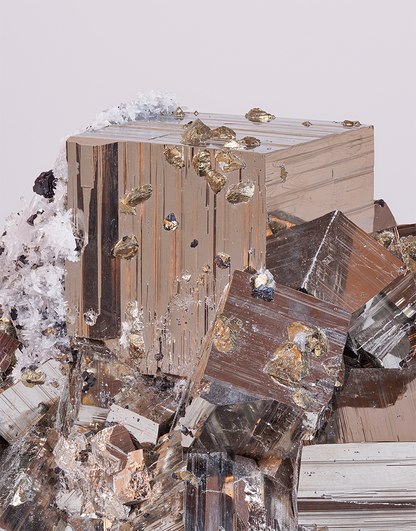 A close-up studio shot of a mineral specimen with a large metallic brown cube surrounded by jagged crystalline fragments and small gold-toned inclusions, set against a plain light gray background.