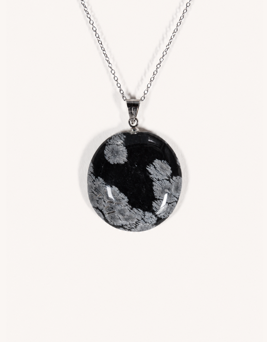 A Natural Snowflake Obsidian Pendant displaying smooth black stone with white cristobalite patches on an 18-inch stainless steel chain.