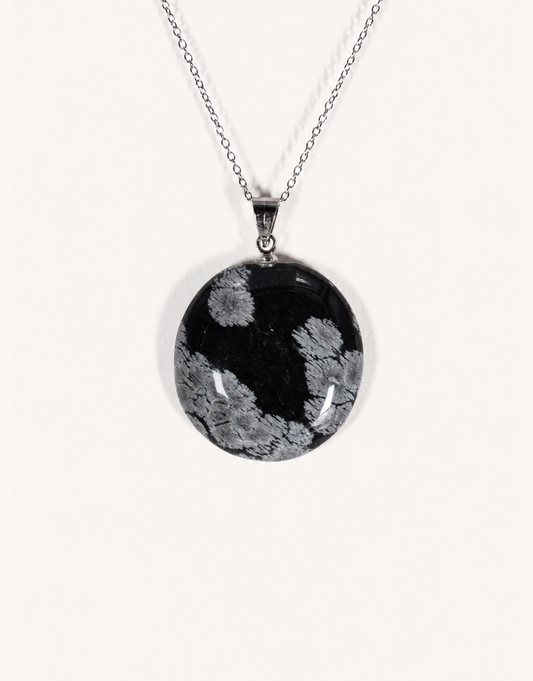 A Natural Snowflake Obsidian Pendant displaying smooth black stone with white cristobalite patches on an 18-inch stainless steel chain.