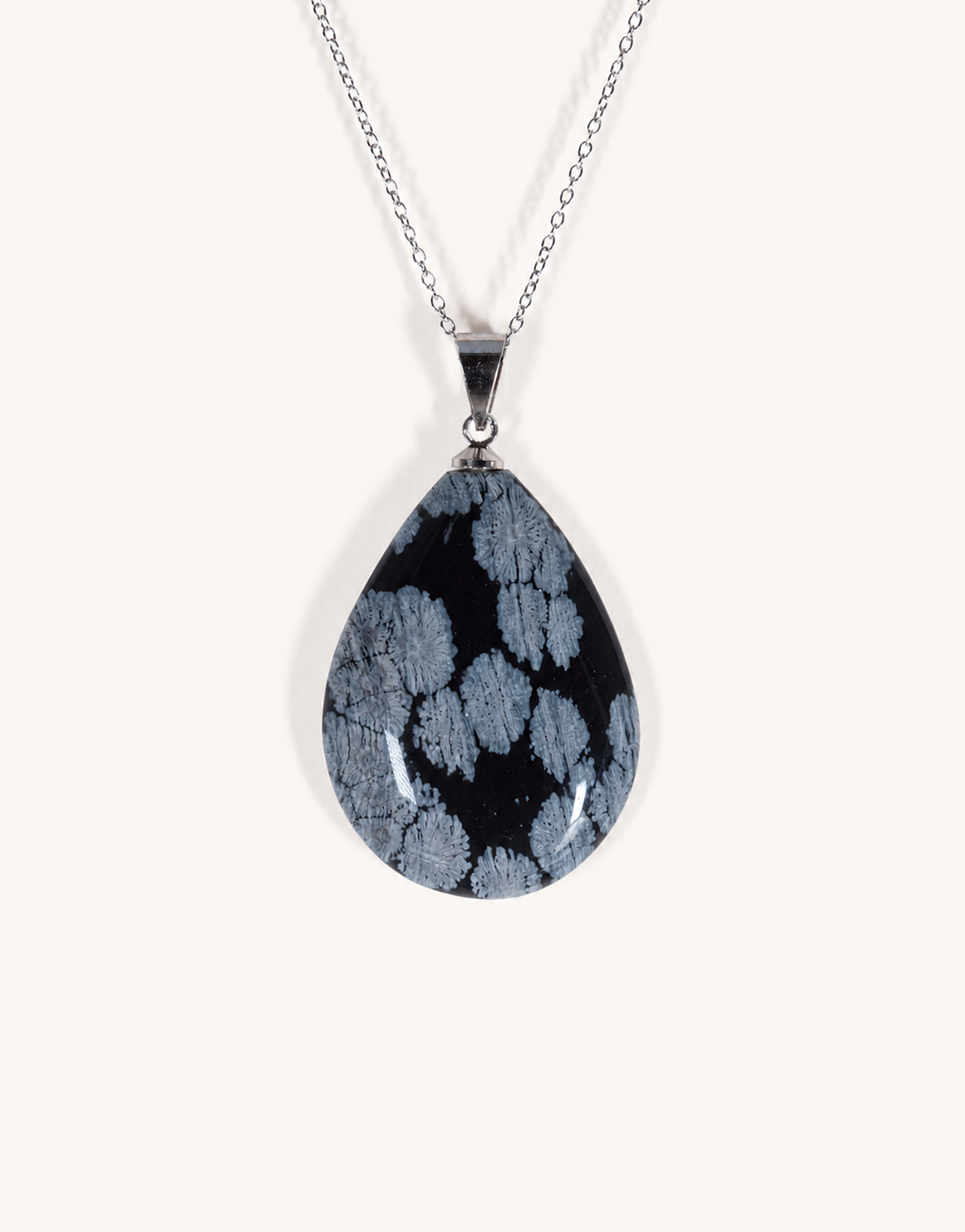 A Natural Snowflake Obsidian Pendant displaying smooth black stone with white cristobalite patches on an 18-inch stainless steel chain.