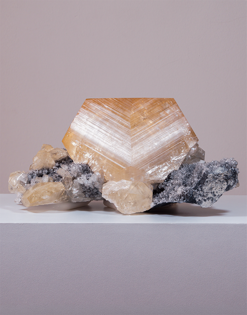 An Orange Yellow Calcite crystal with geometric phantom zoning resting on a dark quartz matrix