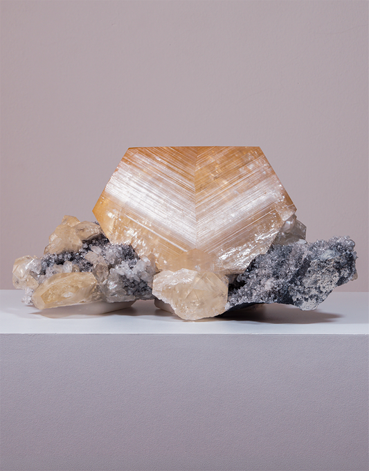 An Orange Yellow Calcite crystal with geometric phantom zoning resting on a dark quartz matrix