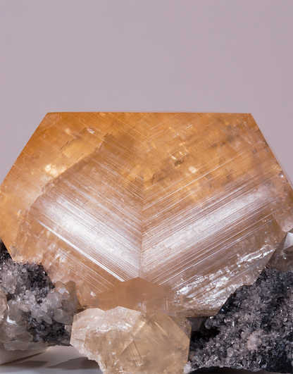 An Orange Yellow Calcite crystal with geometric phantom zoning resting on a dark quartz matrix