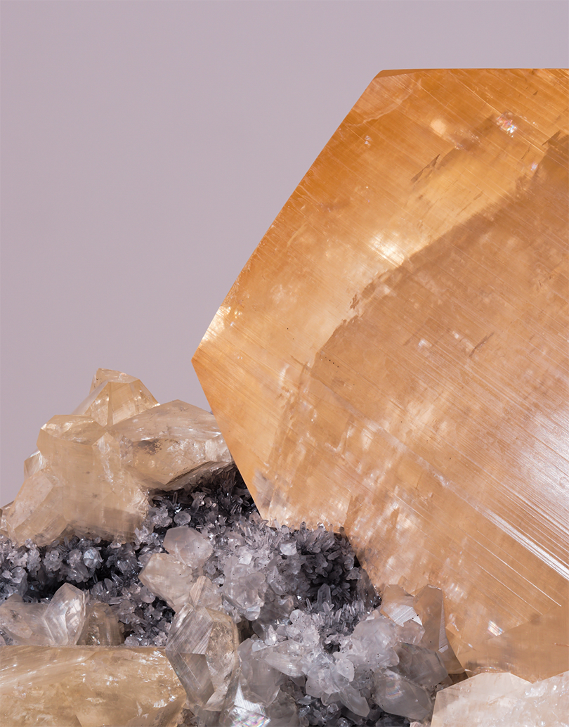 An Orange Yellow Calcite crystal with geometric phantom zoning resting on a dark quartz matrix