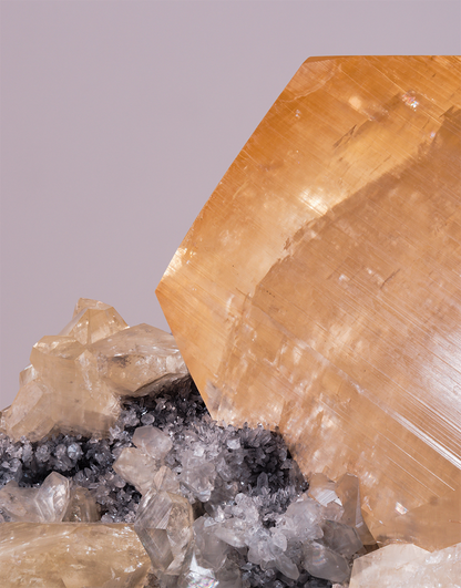 An Orange Yellow Calcite crystal with geometric phantom zoning resting on a dark quartz matrix